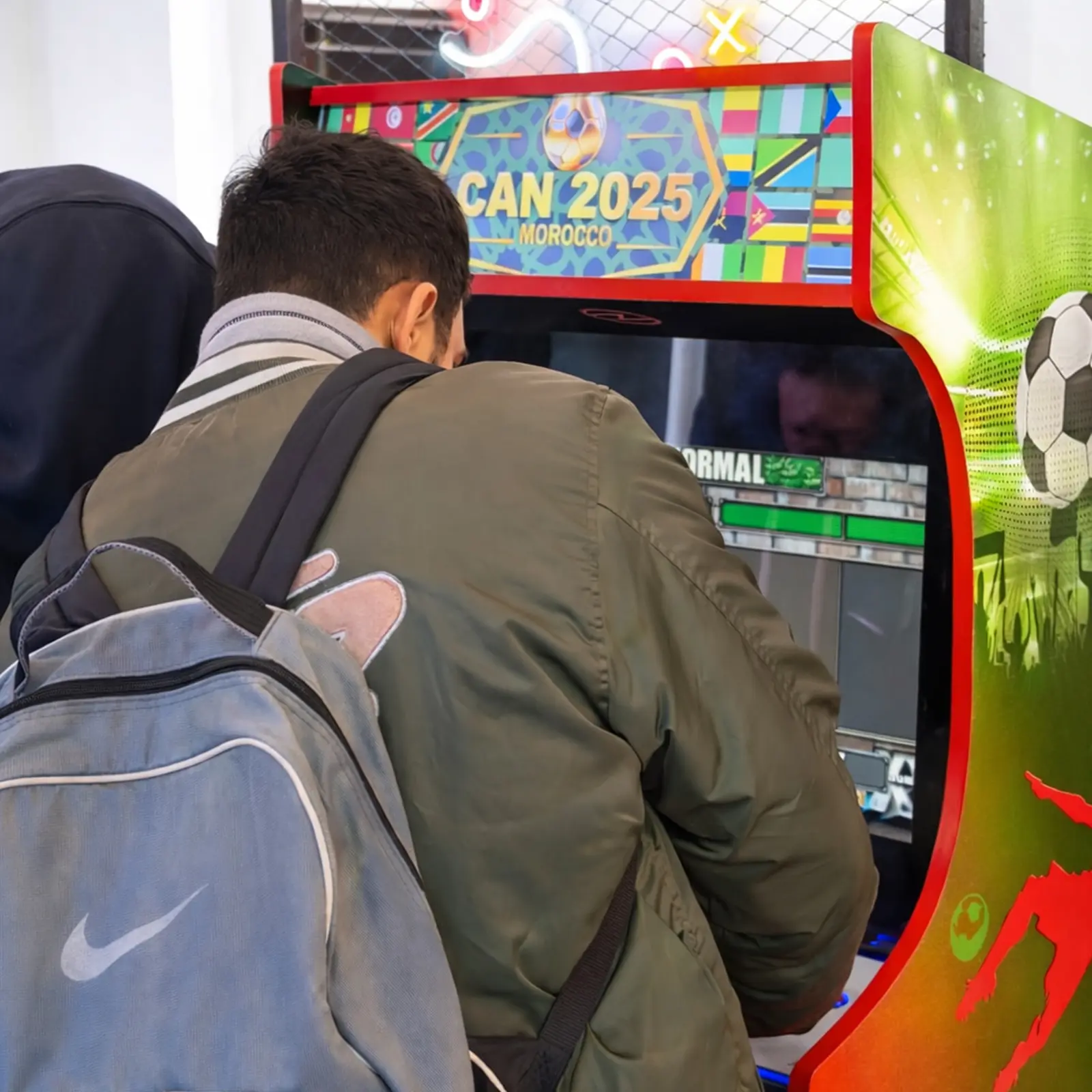 Participant jouant sur une borne d’arcade aux couleurs de la CAN 2025 au sein de la Retro Gaming Exhibition de la Fanzone Ezone à Casablanca, espace gaming aménagé par MG Corp.